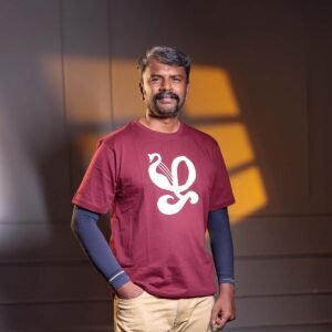 Adult male model with a mustache standing with his hand in his pocket, modeling a maroon Venbaa Zha typography t-shirt with a bold white graphic print under dramatic indoor studio lighting