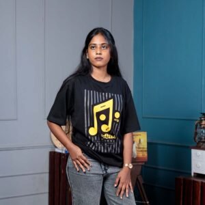 Adult female model posing indoors wearing a black Eevathu Vilakel Athichudi quote t-shirt with a vibrant golden yellow musical note print