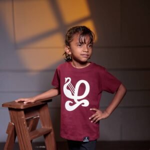 Child wearing a maroon T-shirt featuring beige Tamil- ழ’ typography print inspired by ‘யாழ்’, the ancient Tamil musical instrument.