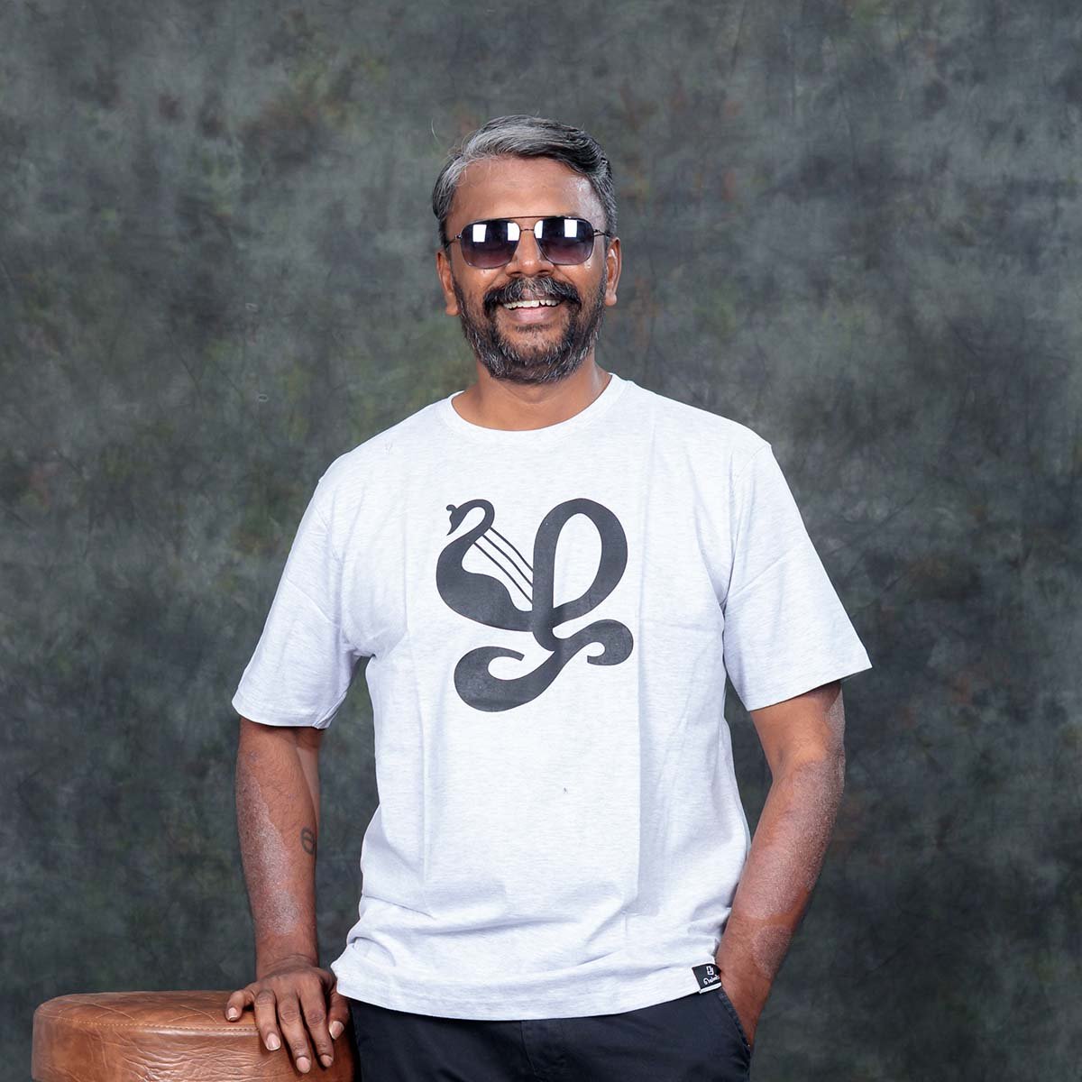 dult male model wearing sunglasses posing indoors in an ecru off-white Venbaa Zha typography t-shirt featuring a black graphic print.
