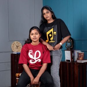 Seated female model looking forward in a maroon Venbaa Zha typography t-shirt alongside a standing model in a black Eevathu Vilakel t-shirt.