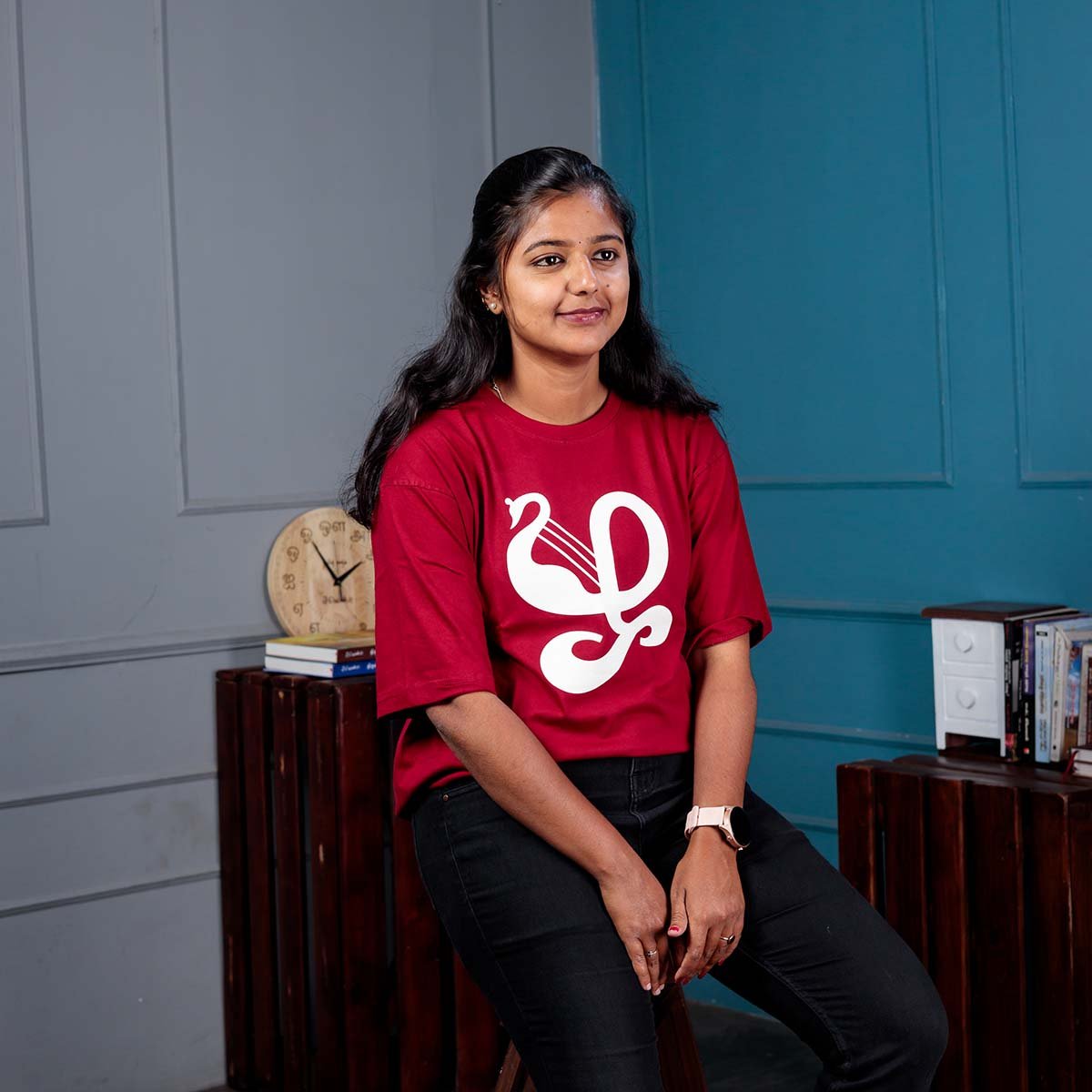 Adult female model smiling while seated indoors, wearing a deep maroon Venbaa Zha typography t-shirt with a white graphic print