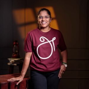Adult female model with glasses smiling directly forward, modeling the maroon 'அ' First Letter (உயிர் எழுத்து) typography Tamil t-shirt.