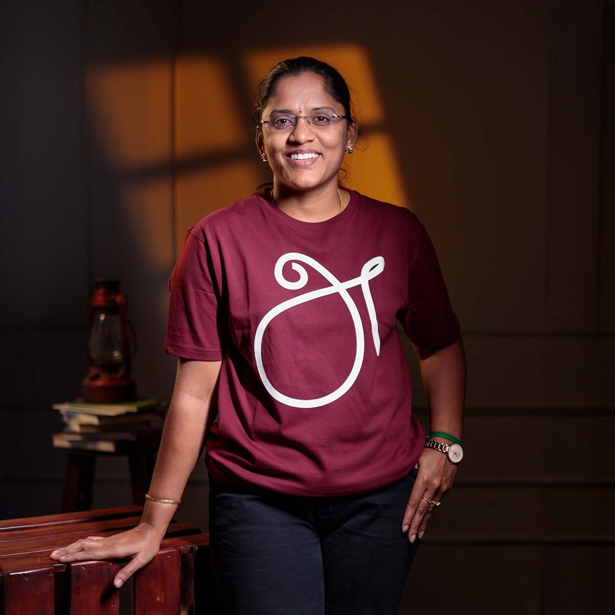 venbaa-a-first-letter-uyir-ezhuthu-tamil-tshirt-maroon-womens-front Adult female model with glasses smiling directly forward, modeling the maroon 'அ' First Letter (உயிர் எழுத்து) typography Tamil t-shirt.