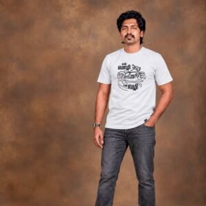 Man with a mustache standing in a studio pose wearing an ecru Venbaa biker t-shirt printed with 'என் மொழி என் வழி' motorcycle graphic and grey jeans