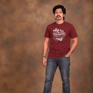 Man standing in a studio pose wearing a maroon Venbaa biker t-shirt printed with white 'என் மொழி என் வழி' motorcycle typography and grey jeans