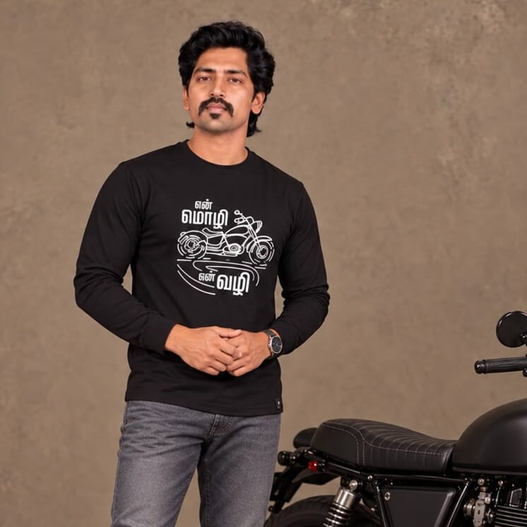 Male model wearing Venbaa En Mozhi En Vazhi black full sleeve Tamil biker T-shirt with white motorcycle graphic, standing beside a black motorcycle.