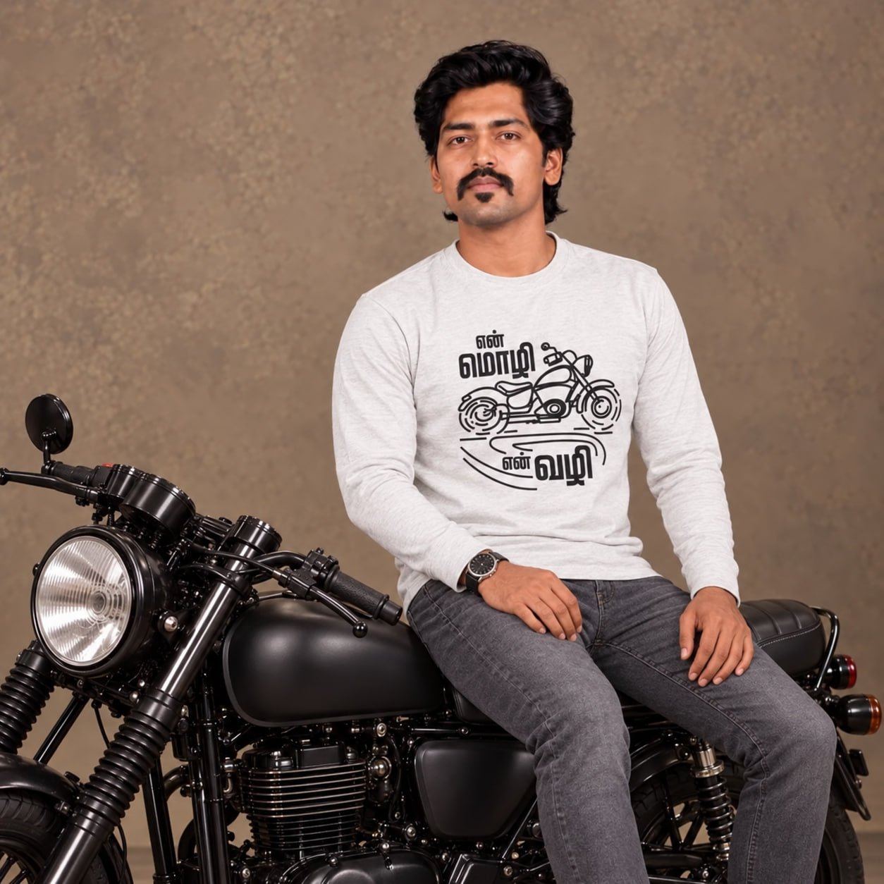 Male model wearing Venbaa's ecru full sleeve En Mozhi En Vazhi Tamil biker T-shirt with black motorcycle graphic, seated on a black motorcycle.