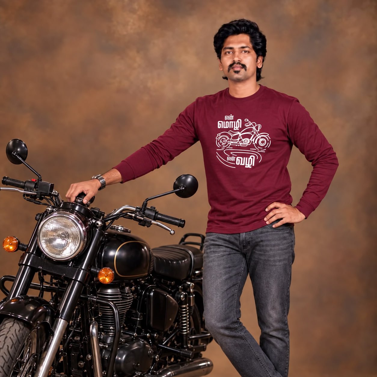 Male model wearing Venbaa's maroon full sleeve En Mozhi En Vazhi Tamil biker T-shirt with a white motorcycle graphic, standing beside a black motorcycle.